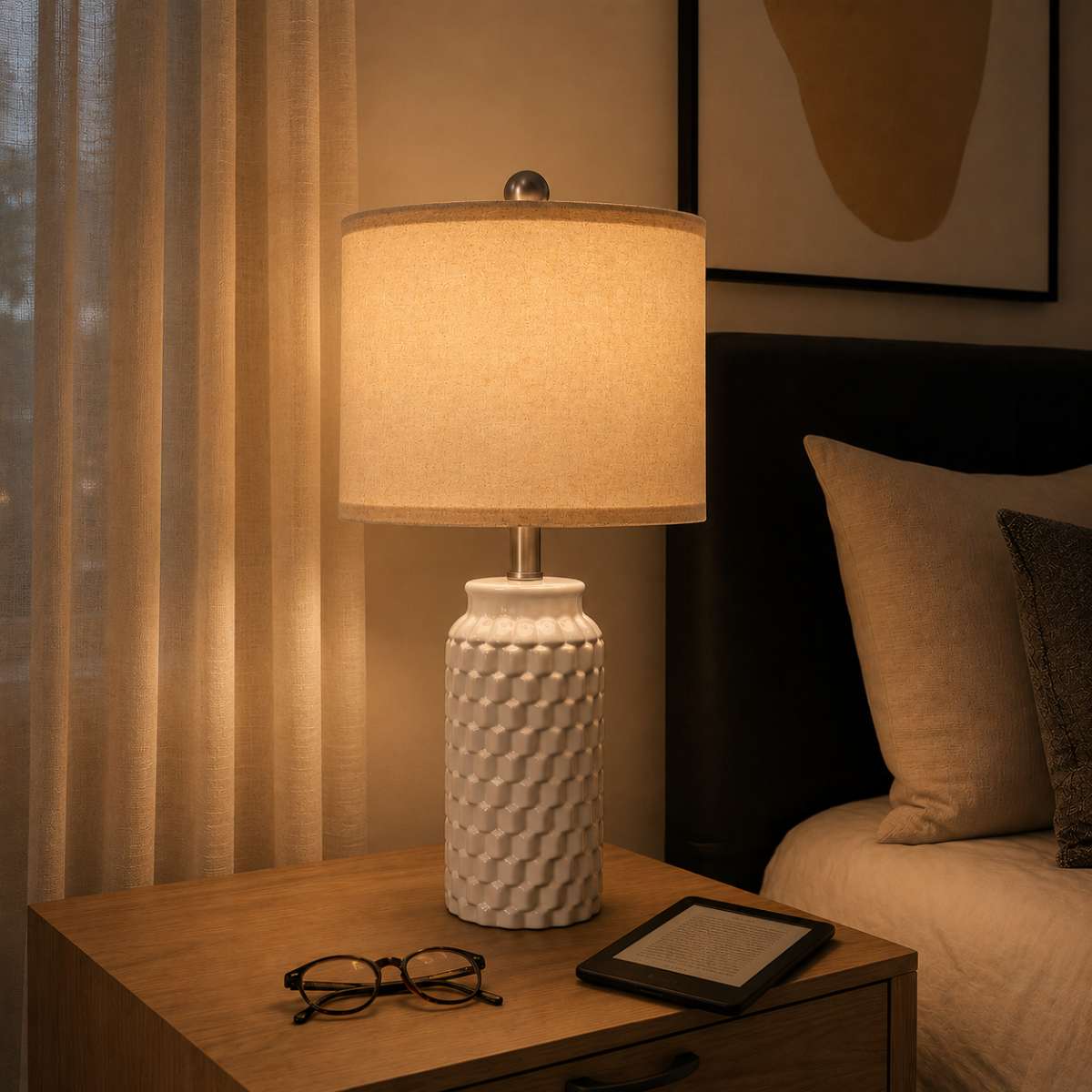Textured white ceramic bedside lamp with warm glow, reading glasses, and kindle