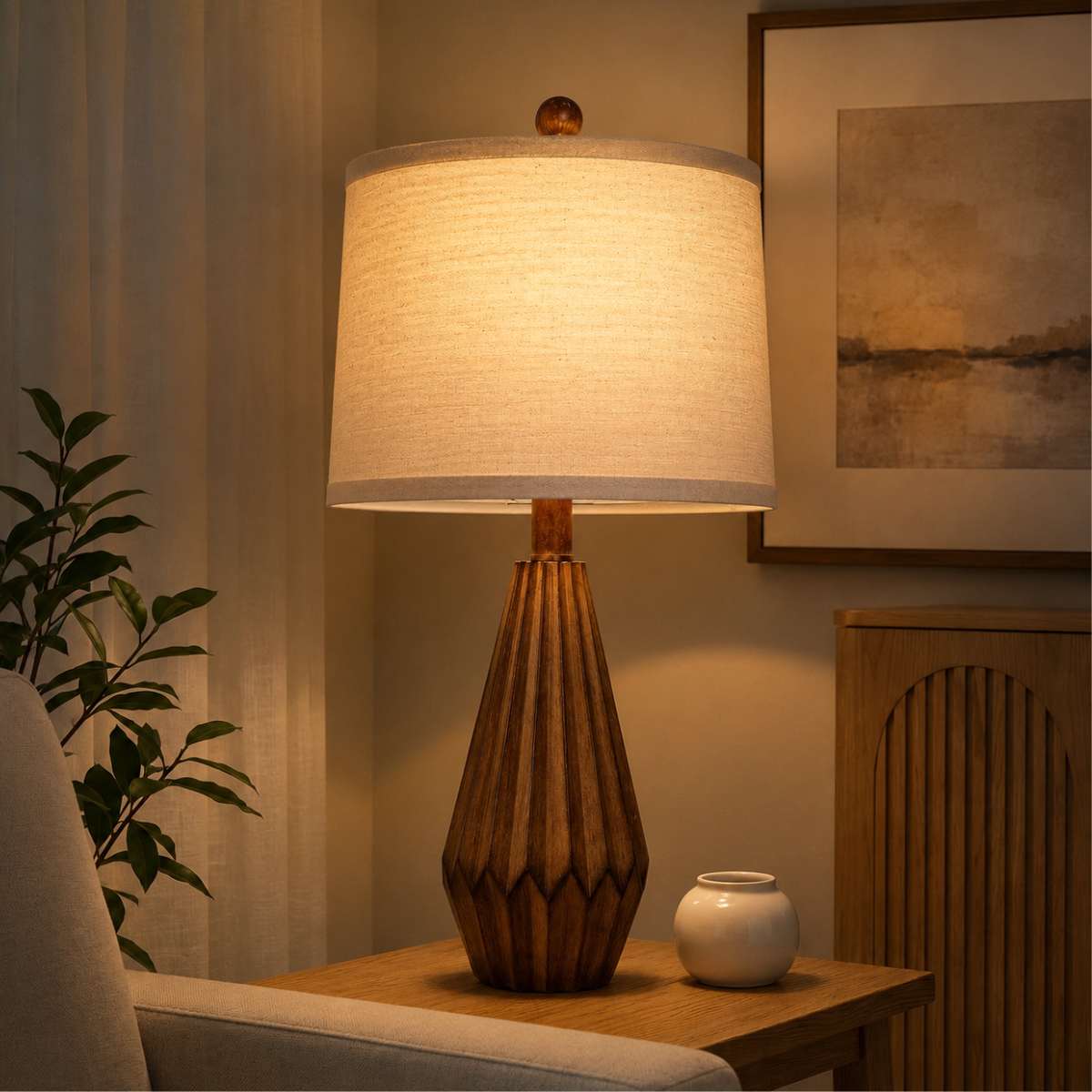 Tall sculptural wood table lamp with linen shade in a cozy living room at night