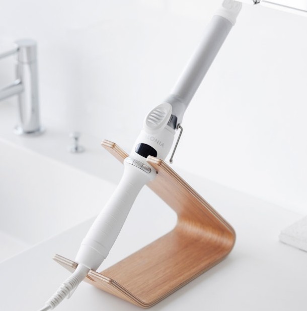 Minimalist wooden stand holding a curling iron on a bathroom counter